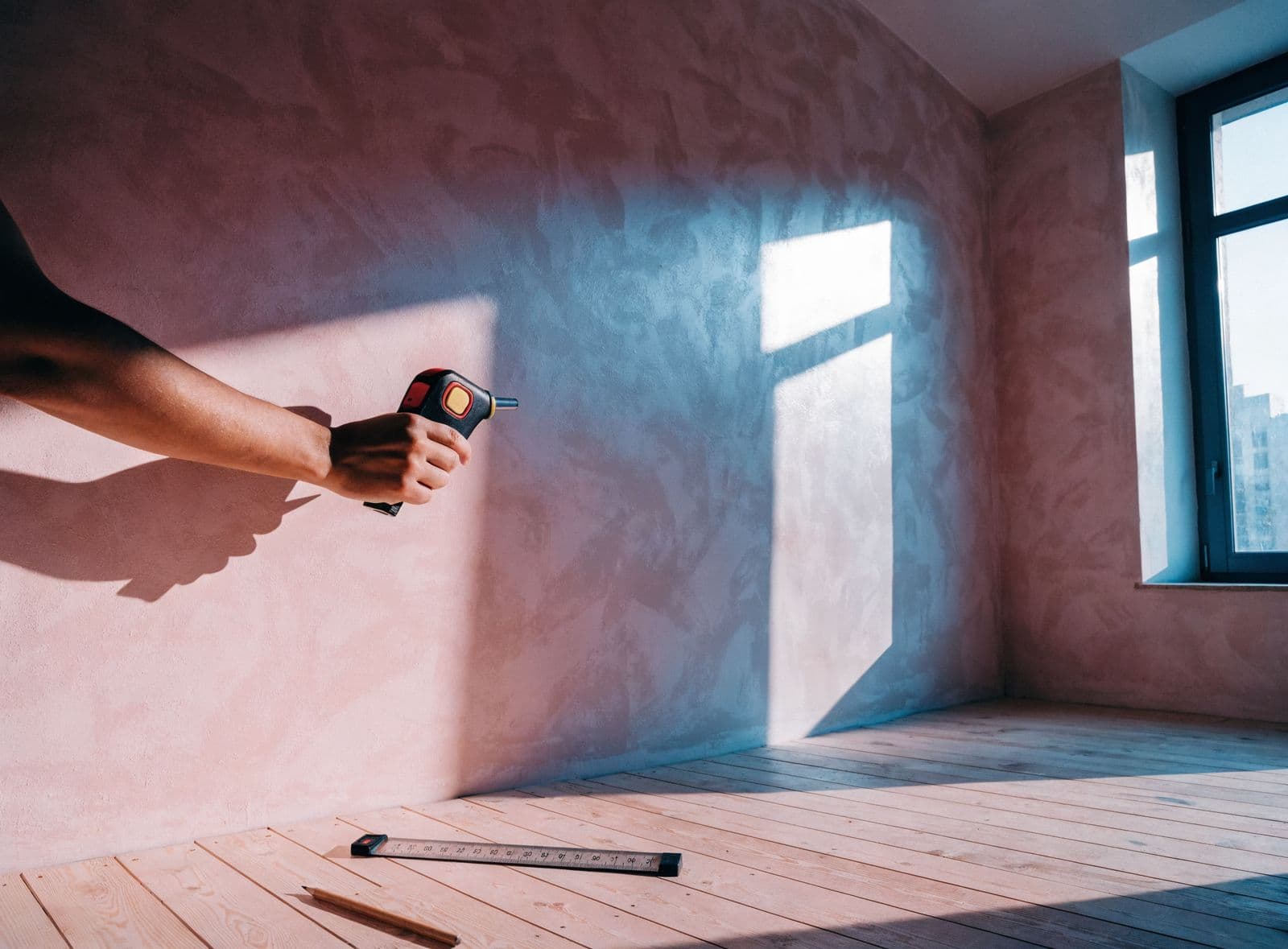 An empty room with fresh plaster, a laser measure held against the wall and a folding rule on the floor.